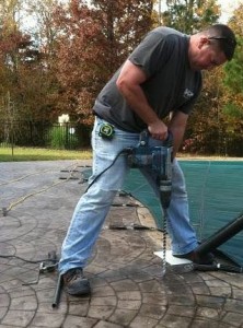 man drilling a pool cover anchor into pool deck, intheswim image